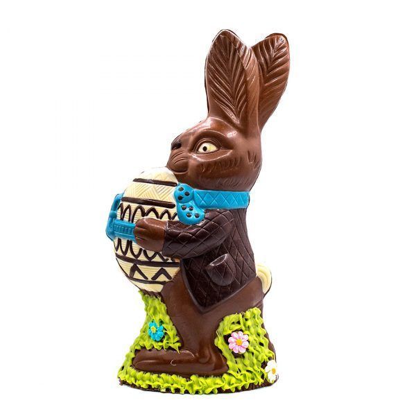 chocolate bunny with a blue scarf holding a yellow easter egg
