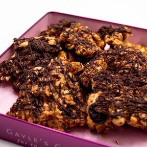pink tin filled with rice krispies, dried Michigan cherries, almonds, cashews, toffee, glaced orange peel, toasted coconut, and a layer of drizzled semisweet chocolate
